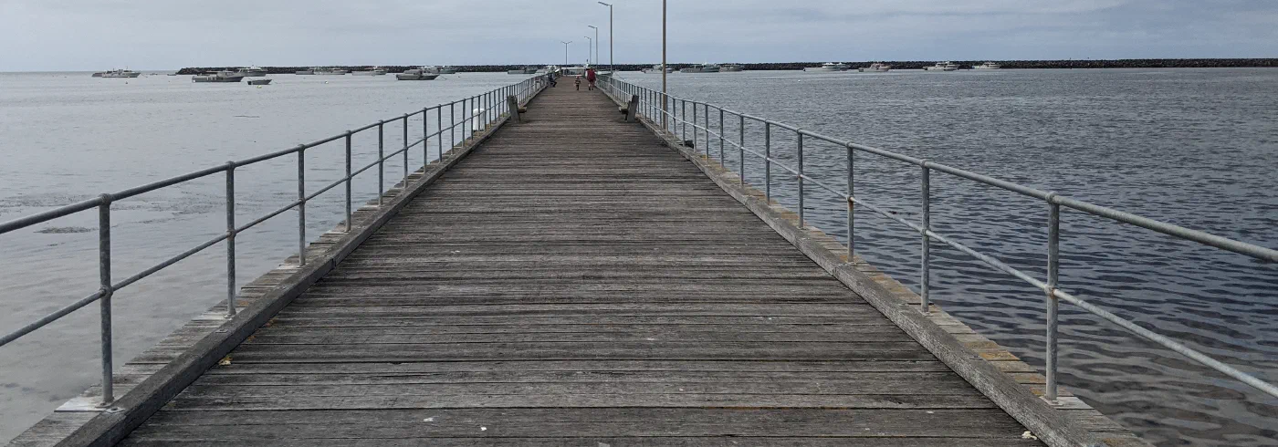 A long wooden jetty reaching out over calm coastal water, boats moored on either side