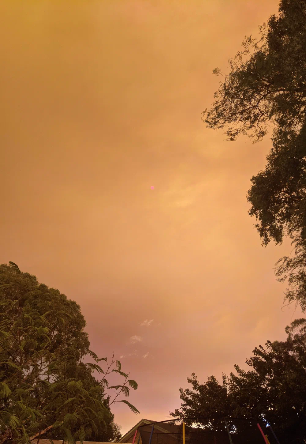 A hazy orange sun glowing through smoke-tinted haze above rooftops