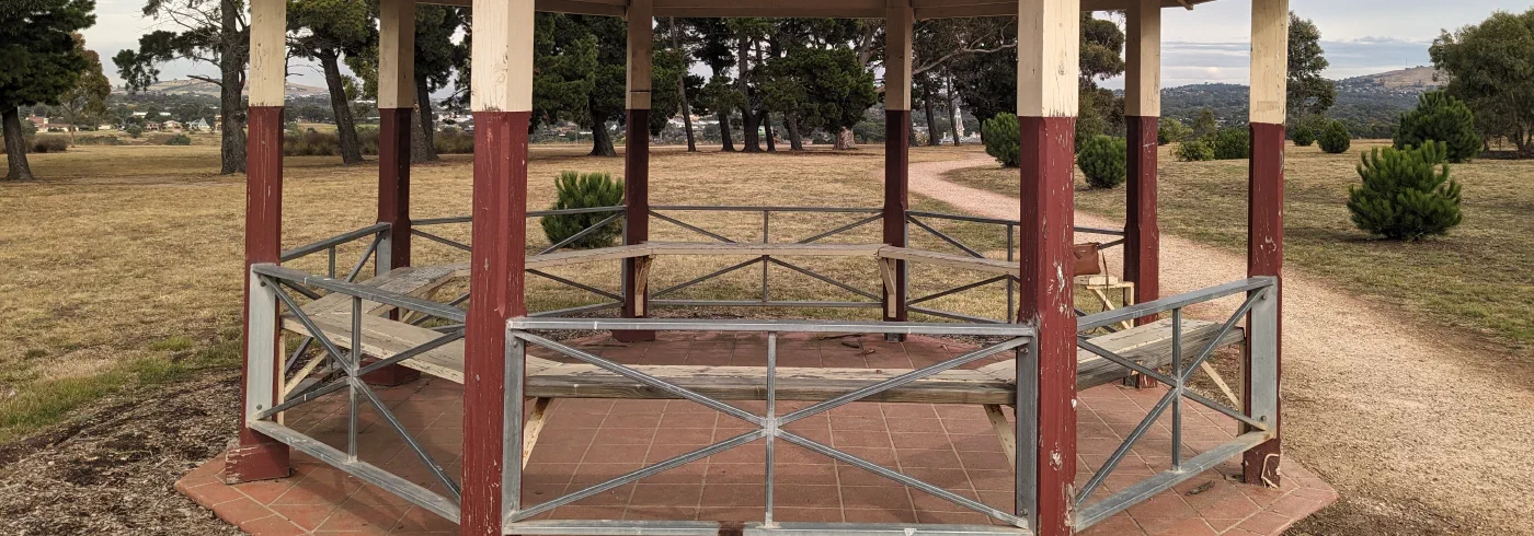 A green-roofed octagonal park gazebo with maroon trim under a clear sky