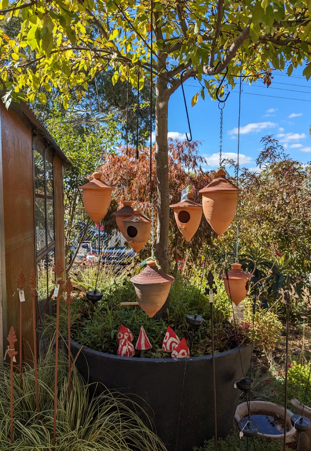 Terracotta birdhouses hanging in a tree above rows of nursery pots