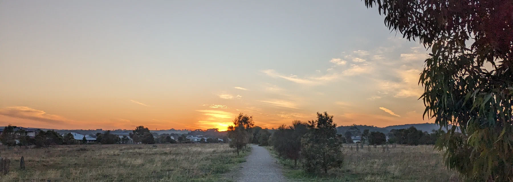 A gravel path through open grassland leading toward a glowing sunset