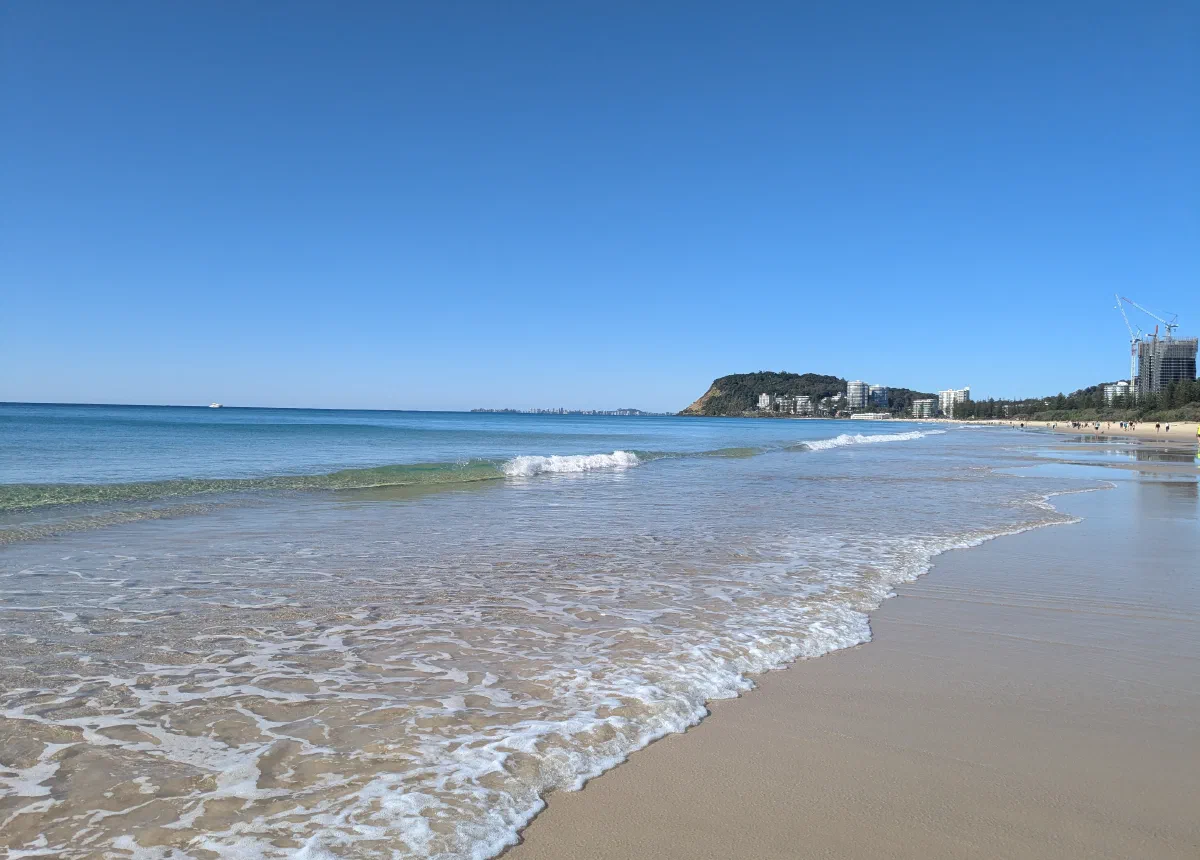 A wide sandy beach curving toward a distant headland and coastal skyline