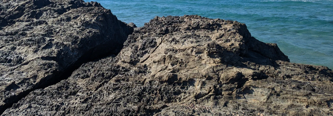 Waves breaking around a dark volcanic rock outcrop at the shoreline