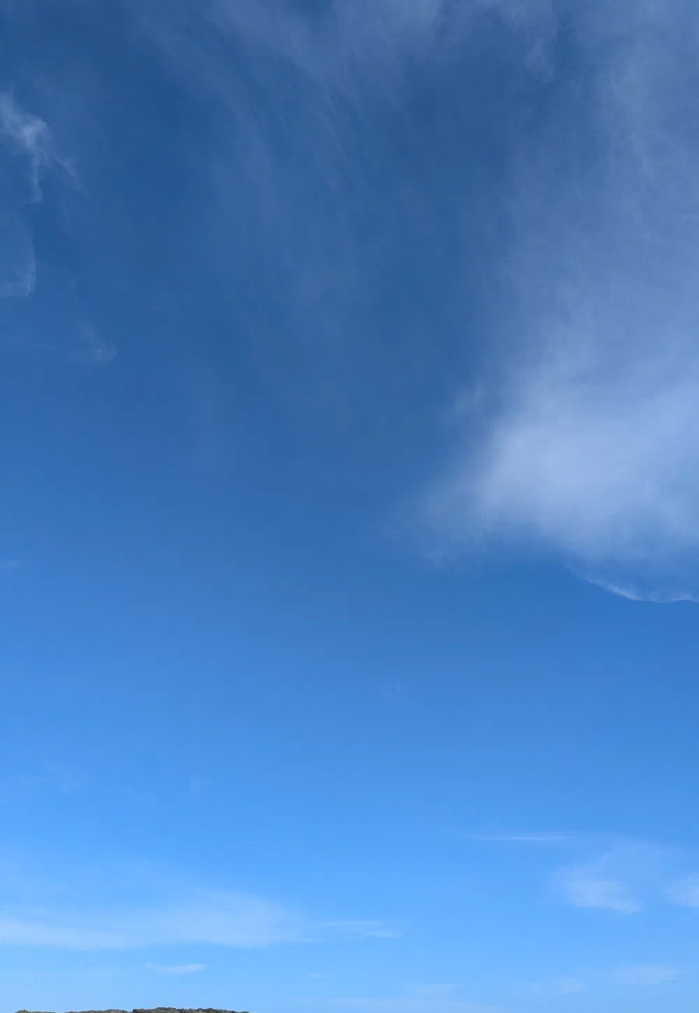 A vast blue sky over a distant headland and thin strip of beach
